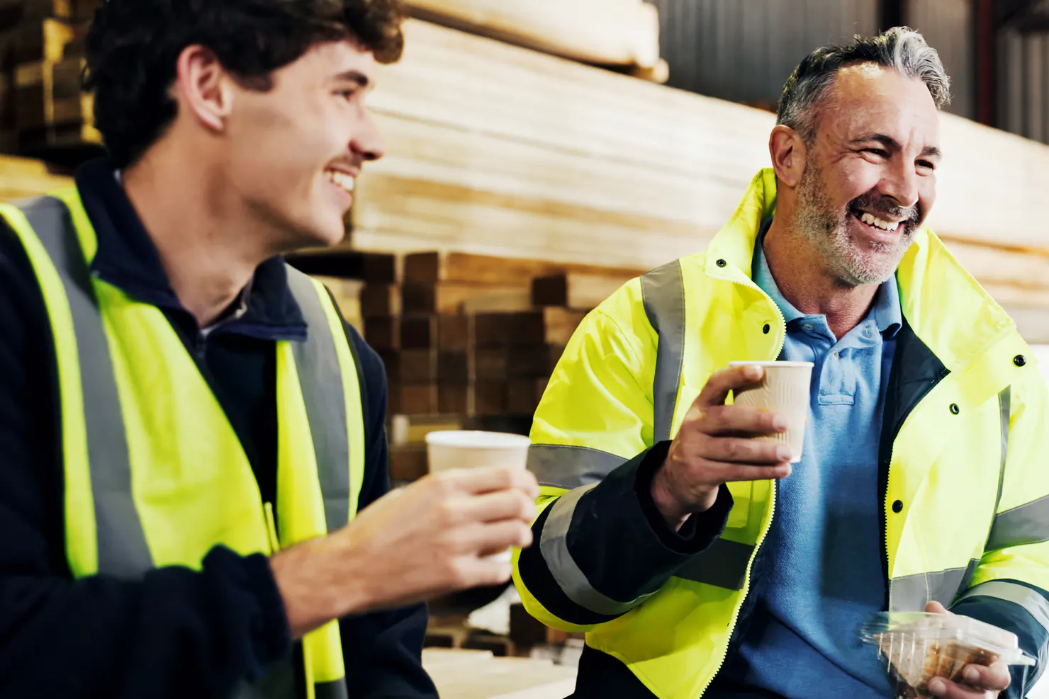 Two colleagues in high-visibility jackets laughing over coffee